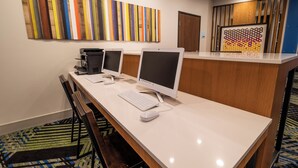 Uma área de recepção de hotel com um balcão comprido, dois monitores, uma impressora e um teclado.