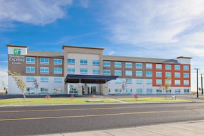 Un hotel Holiday Inn Express & Suites con un diseño moderno, que presenta un techo plano, múltiples ventanas y una entrada cubierta.