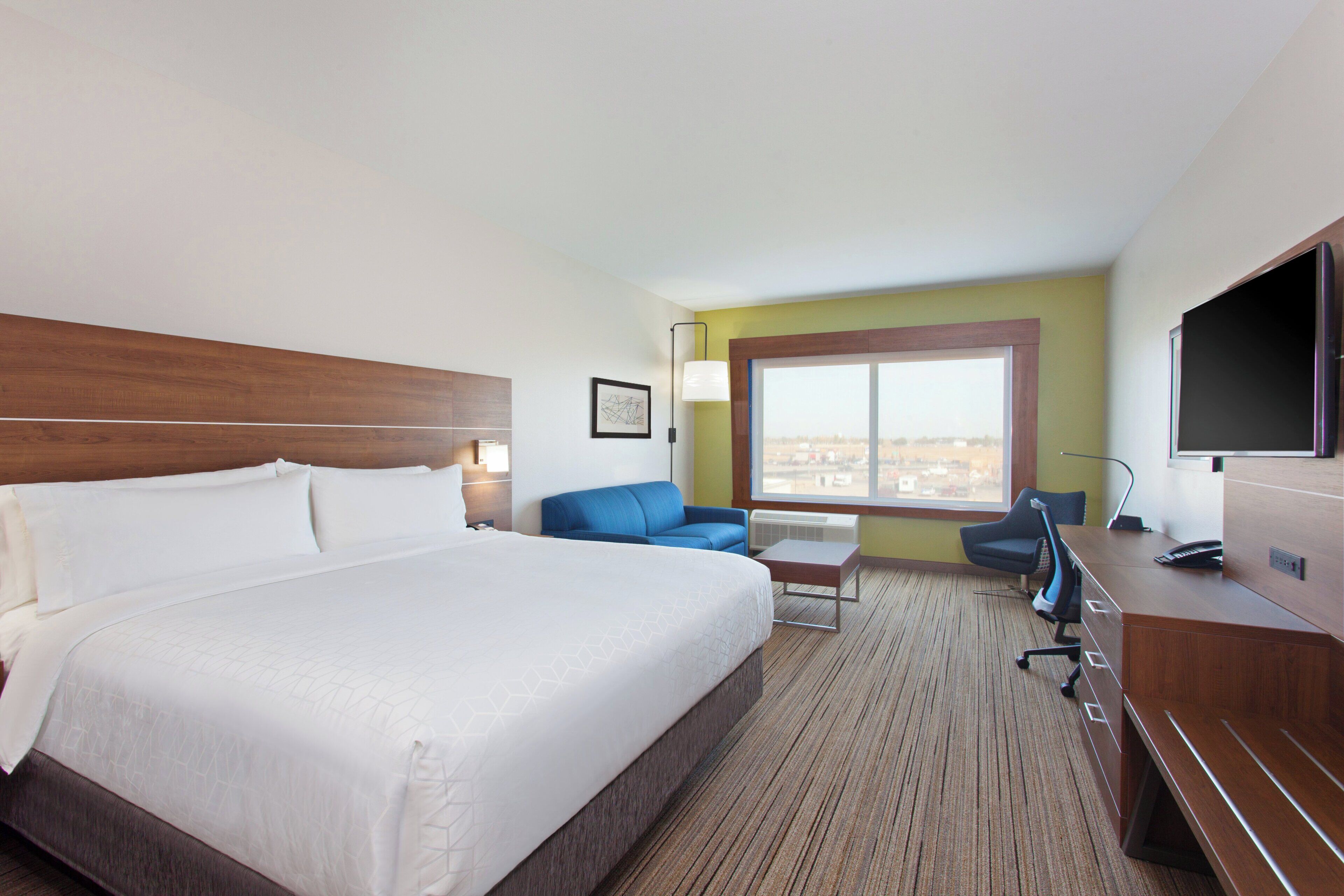 A hotel room with a large bed, a desk, a chair, a TV, and a window with a view.