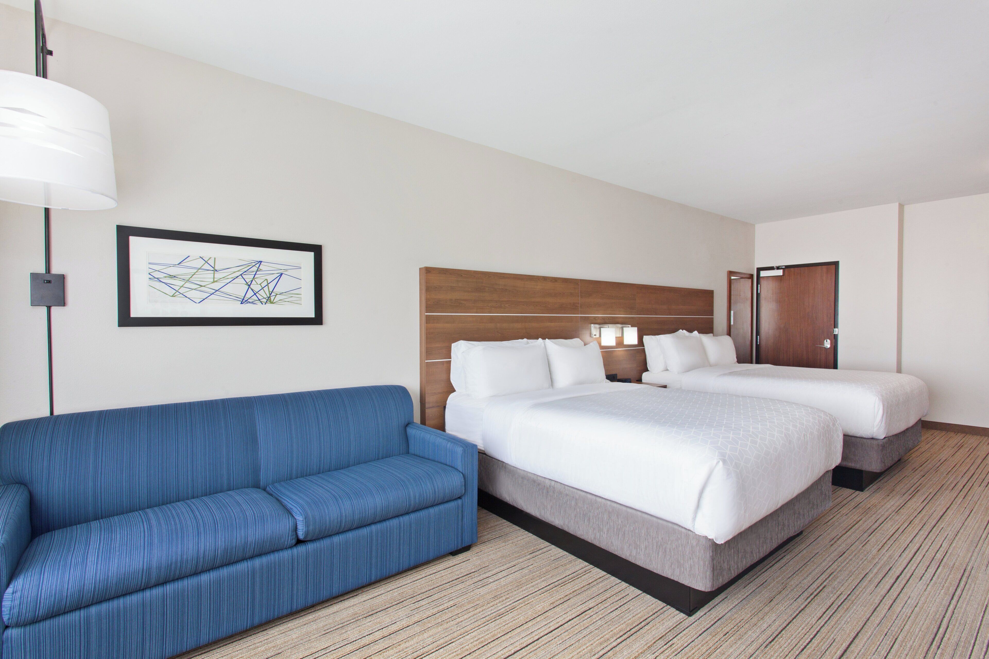 A hotel room with a bed, a blue sofa, and a framed picture on the wall.