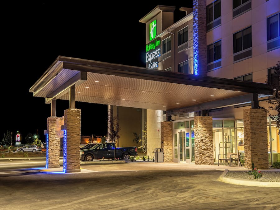 A Holiday Inn Express & Suites building with a covered entrance, stone pillars, and a blue-lit facade.