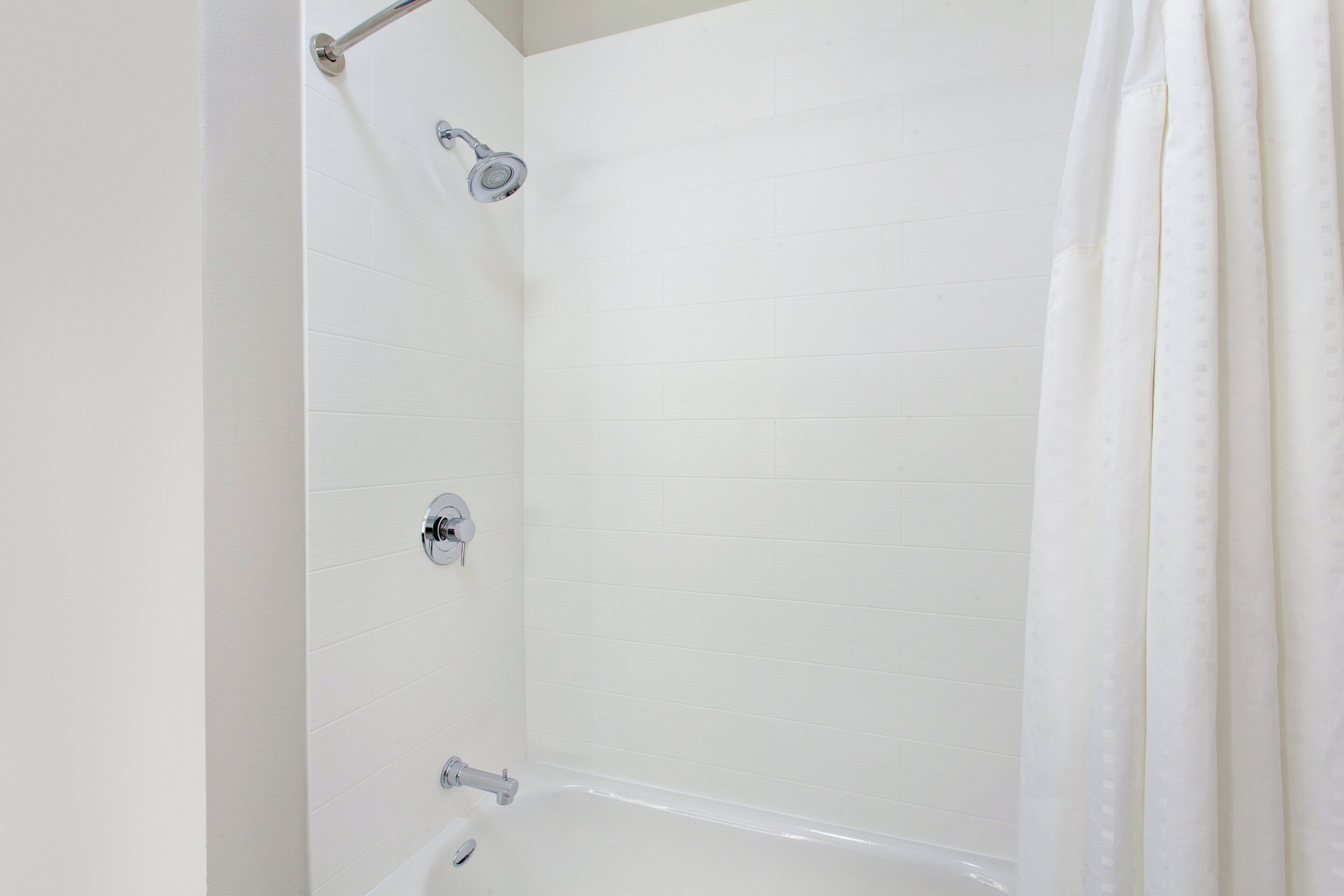 Ducha con azulejos blancos, cabezal de ducha de mano y grifo empotrado.