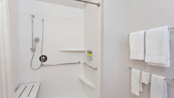 A modern bathroom with a shower, grab bars, and multiple white towels on a rack.