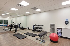Une salle de sport équipée de matériel d’exercice, d’un distributeur d’eau et d’un miroir.
