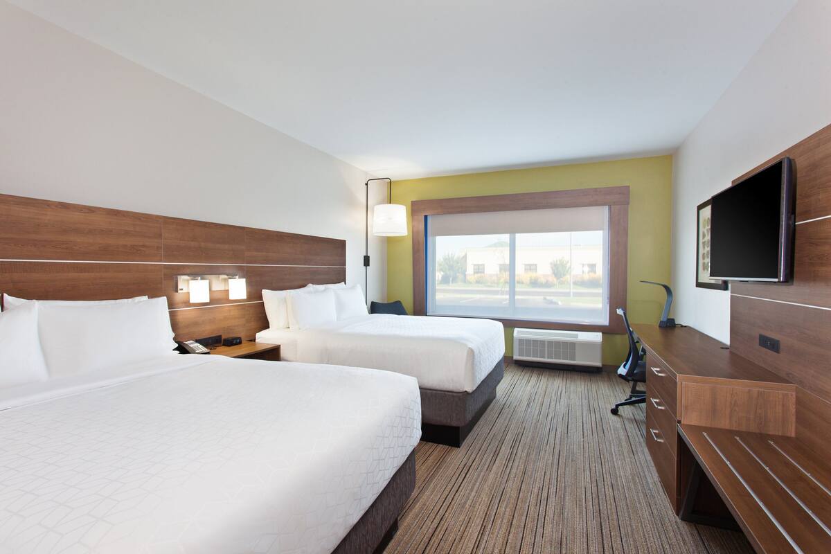 A hotel room with two beds, a TV, a desk, and a window with a view.