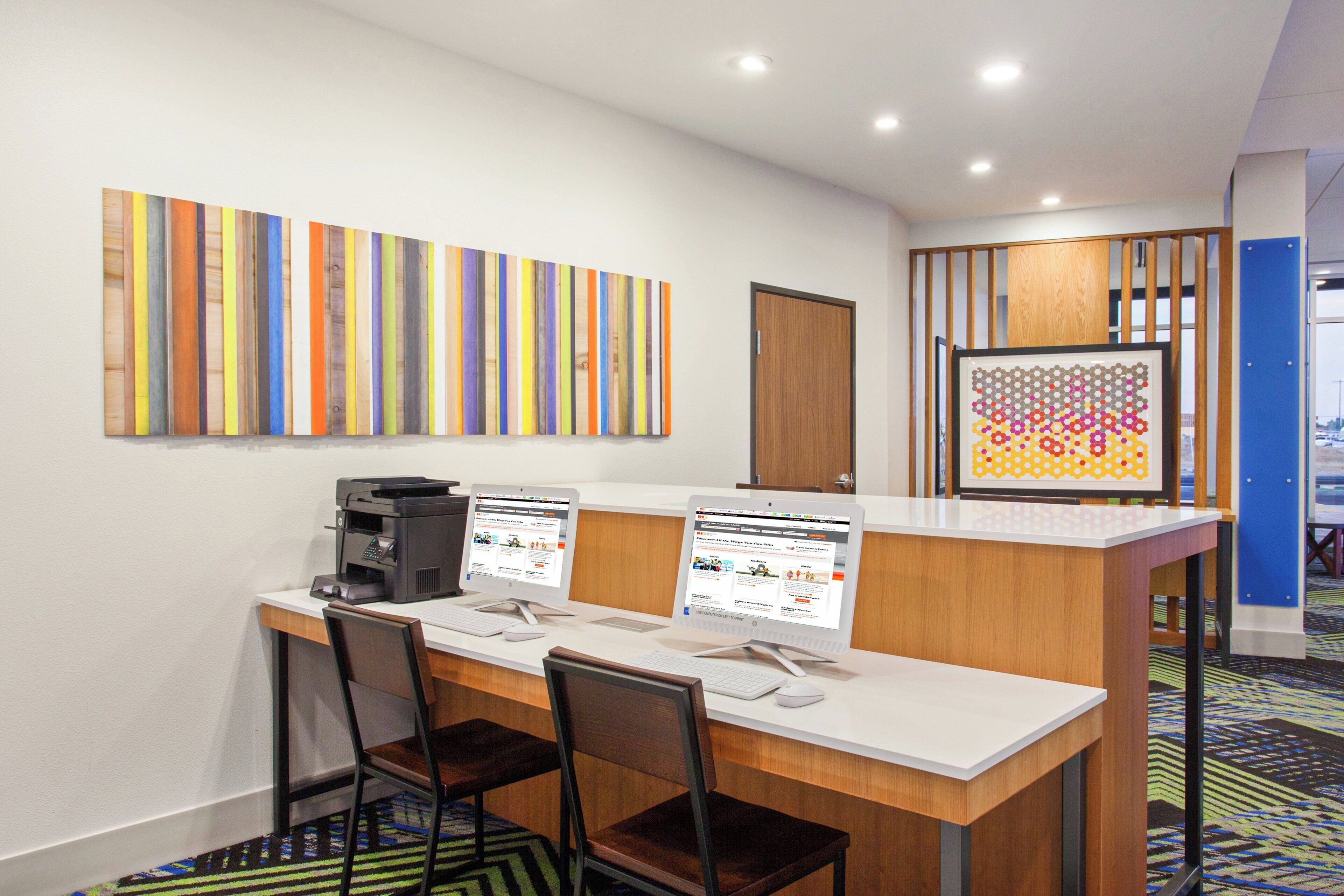 Un mostrador de recepción de hotel con dos computadoras, una impresora y una zona de espera con sillas.