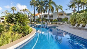 Une piscine avec des chaises longues, des palmiers et un bâtiment en arrière-plan.