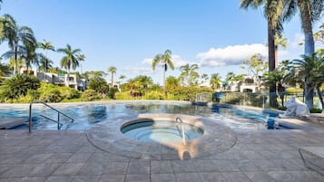 A swimming pool with a hot tub in the center, surrounded by palm trees and a tiled deck.