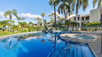 Une piscine à l’eau d’un bleu limpide, entourée de palmiers et bordée d’un bâtiment à la façade blanche.