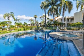 Una piscina con superficie de agua azul cristalina, rodeada de palmeras y un edificio de fachada blanca.