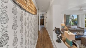Ein Flur mit Tapete mit Ananasmuster, einer Holzbalkendecke und Blick in einen Wohnbereich mit Sofa und Schildkrötenskulptur.