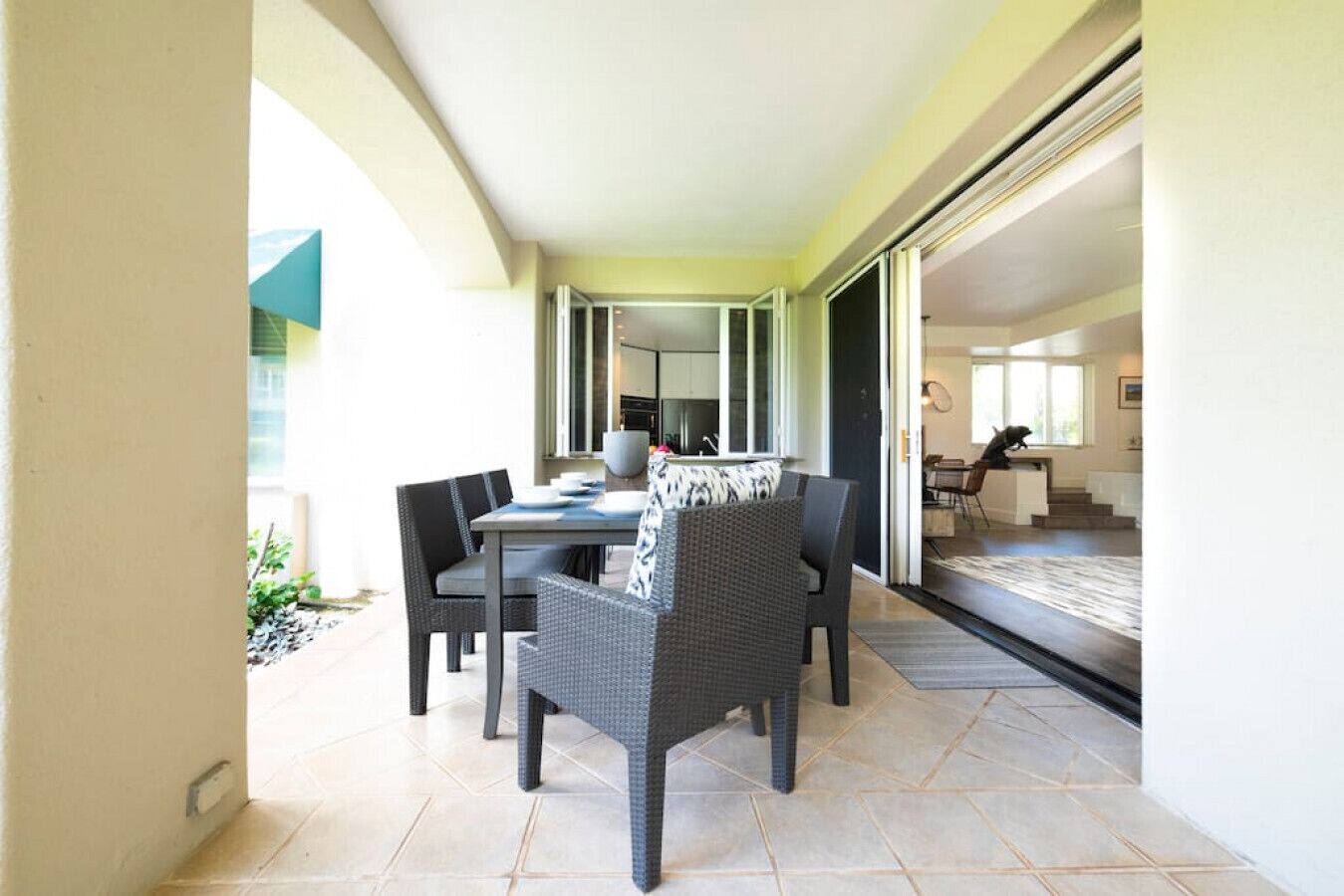 A dining area with a table and chairs, a kitchen in the background, and a view of the outdoors.