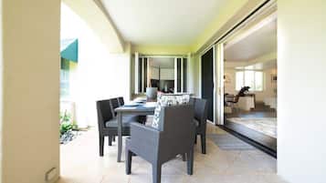 A dining area with a table and chairs, a kitchen in the background, and a view of the outdoors.
