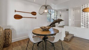 Ein Essbereich mit einem runden Tisch, zwei Stühlen, einer dekorativen Delphin-Skulptur und einer Pendelleuchte.
