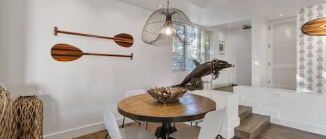 Un coin repas comprenant une table ronde, deux chaises, une sculpture de dauphin décorative et un luminaire suspendu.