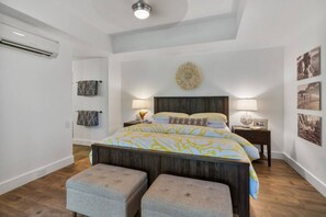 A bedroom with a large bed, two bedside tables, a wall-mounted air conditioner, and a ceiling light.