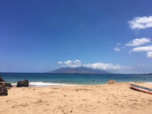 A beach with a clear sky, a mountain in the background, and a surfboard on the sand. - StunningReno*Palms in Wailea Condo-Beach*Golf*Pool (Wailea-Makena)