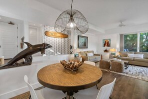 Ein modernes Wohnzimmer mit einem runden Holzes Esstisch, weißen Stühlen, einer großen Fischskulptur und einer Hängeleuchte.