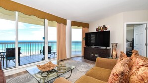 A living room with a glass coffee table, a sofa, a television, and a view of the ocean through large sliding doors. - Beachfront condo w/tile, hardwoods, & a private balcony! (Destin)