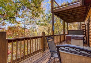 A wooden deck with a hot tub, a chair, and a view of autumn trees.