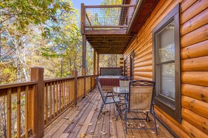 A wooden deck with a covered seating area, a window, and a view of the surrounding trees.