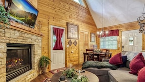 A cozy log cabin interior with a stone fireplace, wooden walls, a dining area, and a comfortable seating space. - Amberwood, “Cozy Cabin Retreat in the Smokies – Comfort & Fun for All” (Sevierville)