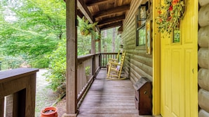 A wooden porch with a yellow door, rocking chairs, and a hanging plant. - Amberwood, “Cozy Cabin Retreat in the Smokies – Comfort & Fun for All” (Sevierville)