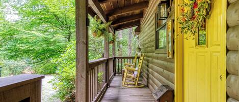 A wooden porch with a yellow door, rocking chairs, and a hanging plant.