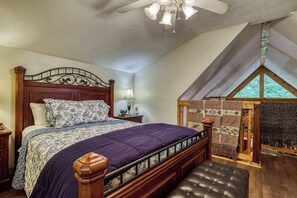 Un dormitorio con una cama grande, cabecera de madera, una mesita de noche con lámpara, un banco y vistas al exterior a través de una ventana.