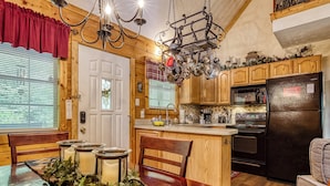 A cozy kitchen with wooden cabinets, a black refrigerator, and a chandelier. - Amberwood, “Cozy Cabin Retreat in the Smokies – Comfort & Fun for All” (Sevierville)