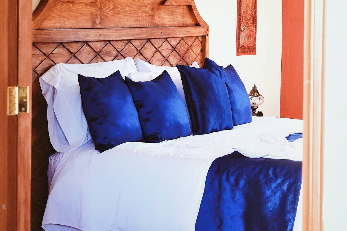 A bed with a wooden headboard, white and blue bedding, and a red accent wall.