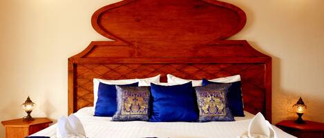 A bed with a wooden headboard, blue and patterned pillows, white bedding, and two bedside tables with lamps.