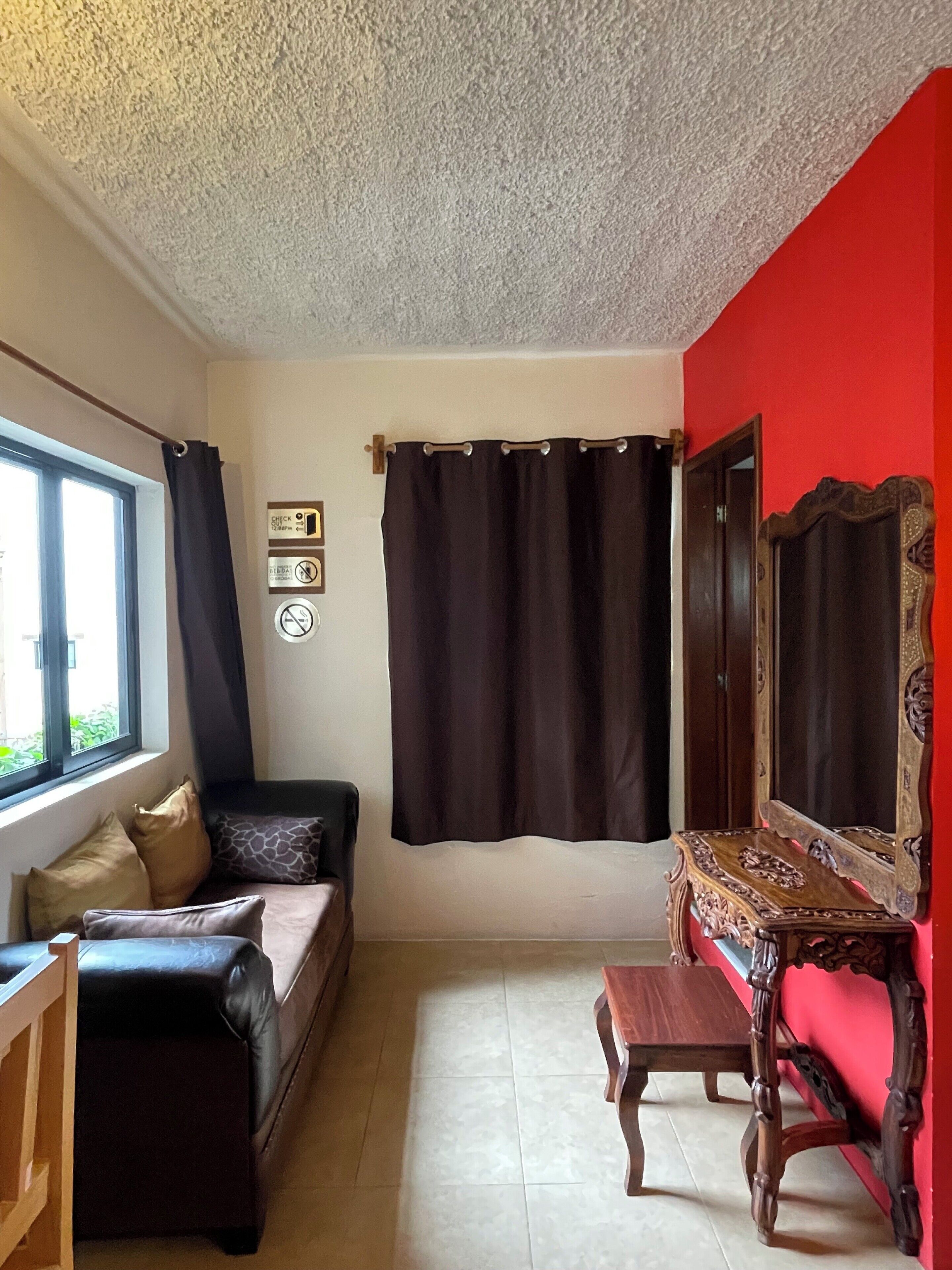 A room with a red wall, a black sofa, a wooden table, and a mirror.