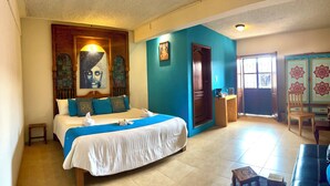 Una habitación de hotel con una cama, una mesita, una silla y una puerta que da a otra estancia.