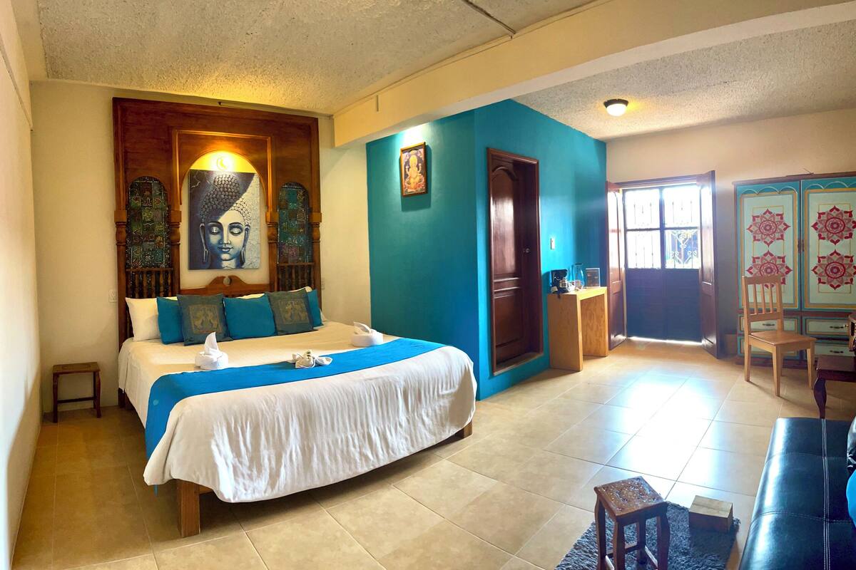 A hotel room with a bed, a small table, a chair, and a door leading to another room.