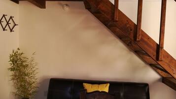 A room with a wooden staircase, a black leather sofa with a yellow pillow, and a bamboo plant.