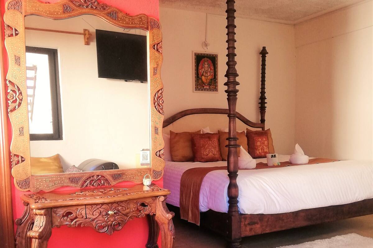 A bedroom with a four-poster bed, a wooden desk with a chair, and a large mirror.