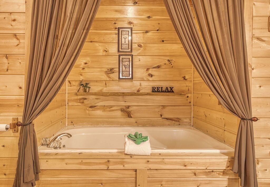 A wooden cabin room with a bathtub, curtains, and a towel with a plant.