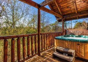 Una terraza de madera con un jacuzzi, barandas de madera y un banco.