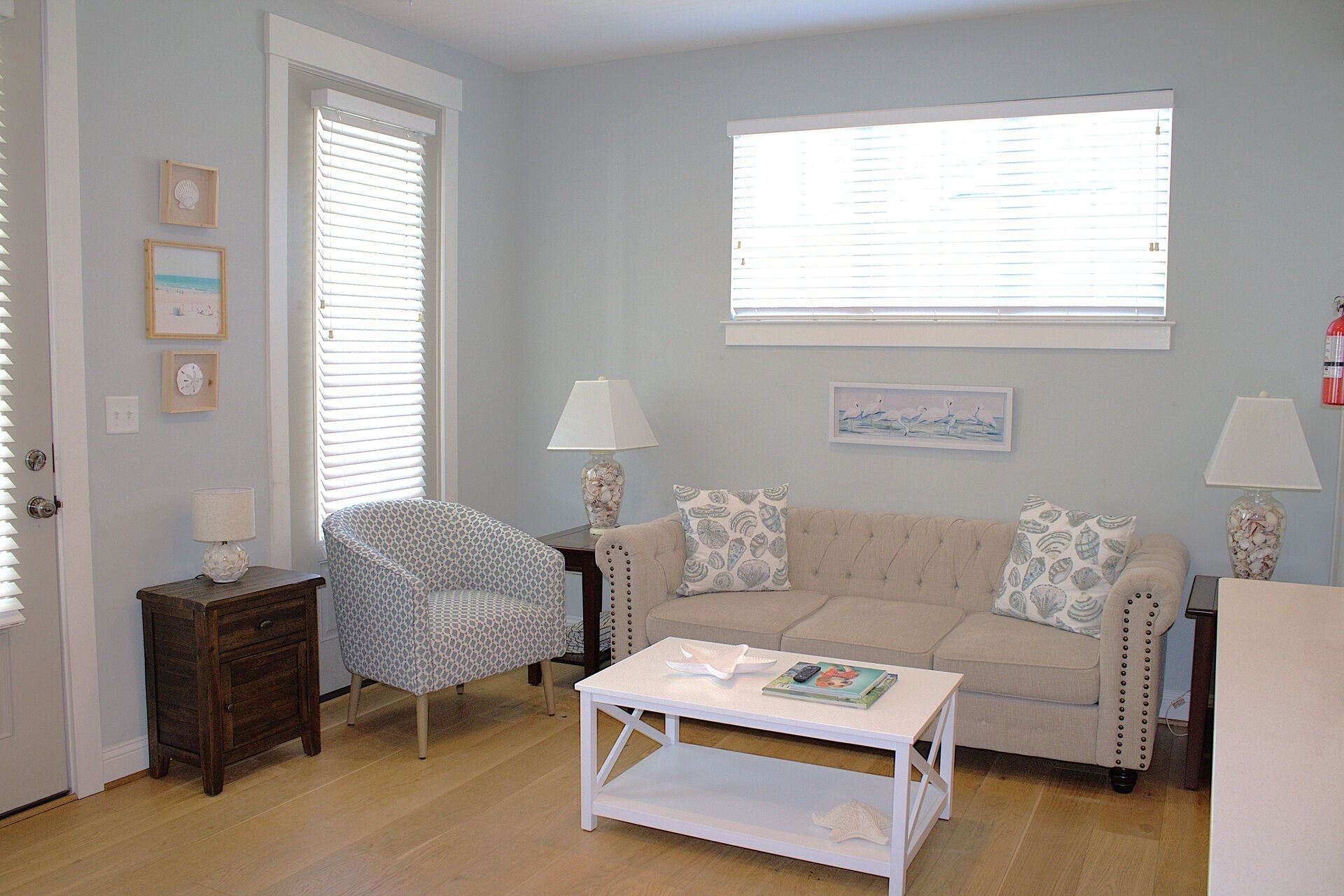 A living room with a beige sofa, two lamps, a coffee table, and a window with blinds.