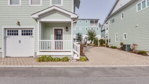 A row of light green two-story houses with a central porch, a garage, and a paved driveway. - 2BR Virginia Beach townhouse with king suite, balcony, WiFi, parking. (Virginia Beach)