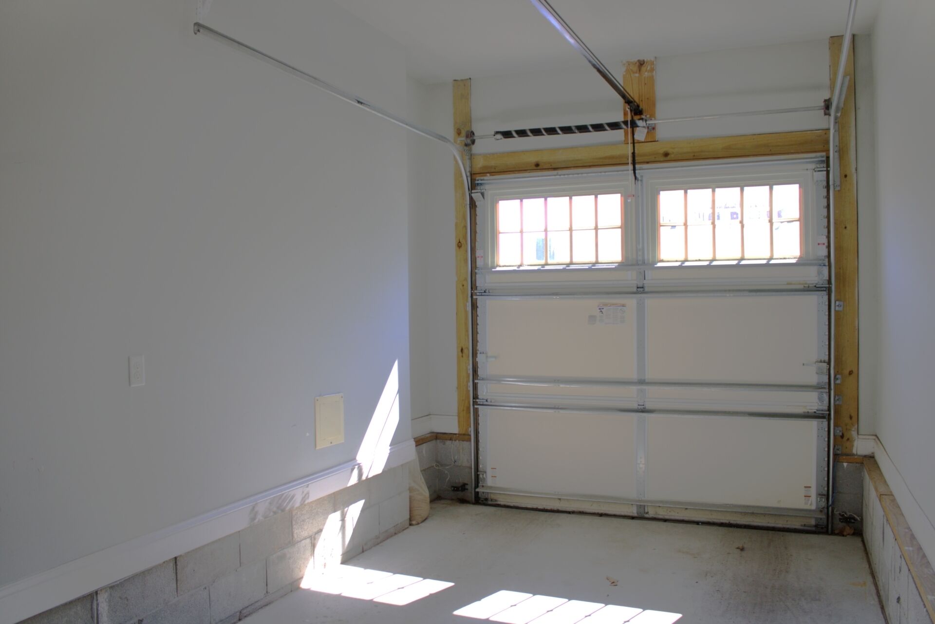 Un garaje con una gran puerta metálica, suelo de concreto y techo de vigas de madera.