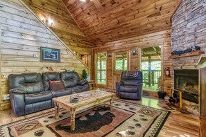 Cozy cabin interior with a high ceiling, stone fireplace, and large window.