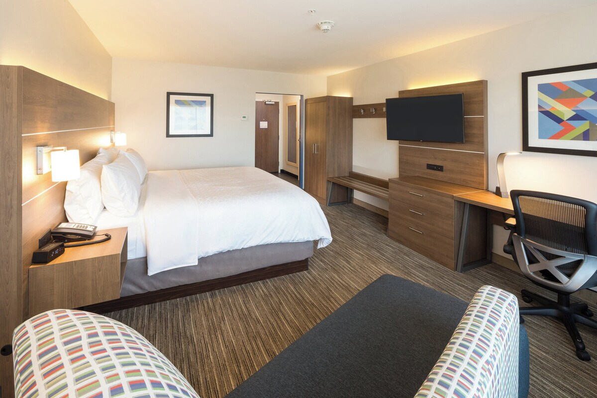 A hotel room with a bed, bedside tables, a desk, a chair, a television, and a framed picture on the wall.