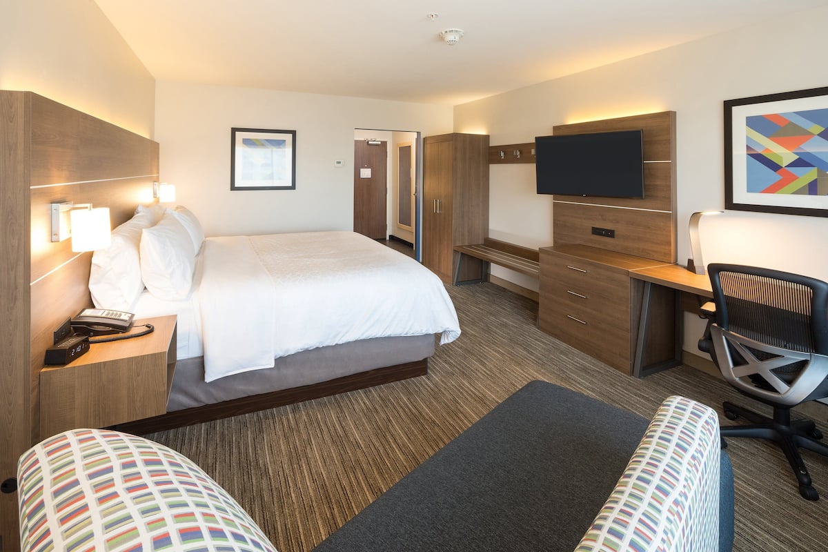 A hotel room with a large bed, a desk with a flat-screen TV, a chair, and a small couch.