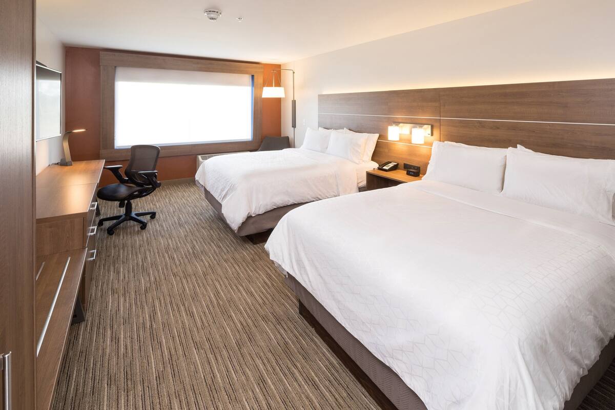 A hotel room with two beds, a desk, a chair, and a large window.