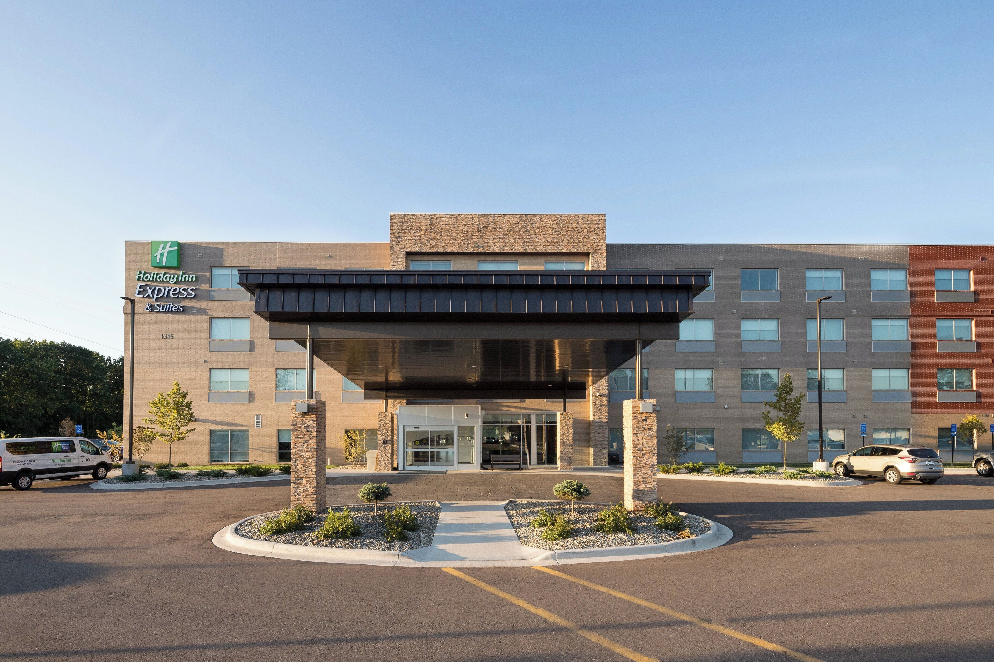 A Holiday Inn Express building with a modern entrance, parking area, and a clear sky.