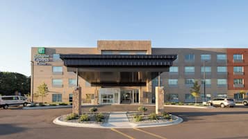 A Holiday Inn Express building with a modern entrance, parking area, and a clear sky.