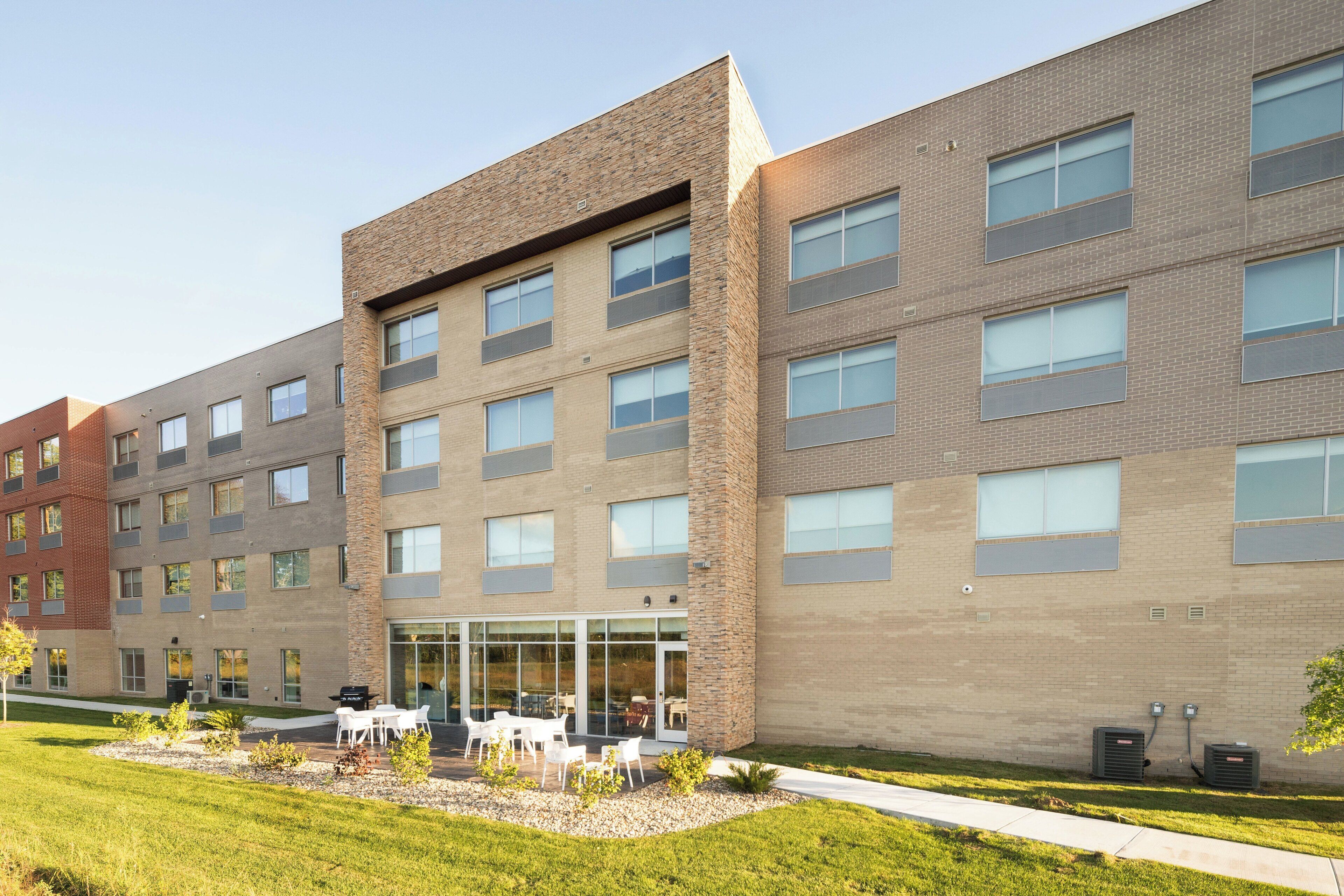 Un immeuble à plusieurs étages doté d’une architecture moderne, caractérisé par un mélange de façades en brique et en béton, de grandes fenêtres et une entrée centrale avec des portes en verre.