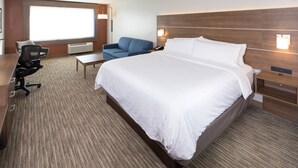 A hotel room with a large bed, a desk with a chair, a blue sofa, and a large window providing natural light. - Holiday Inn Express and Suites Kalamazoo West by IHG (Kalamazoo)